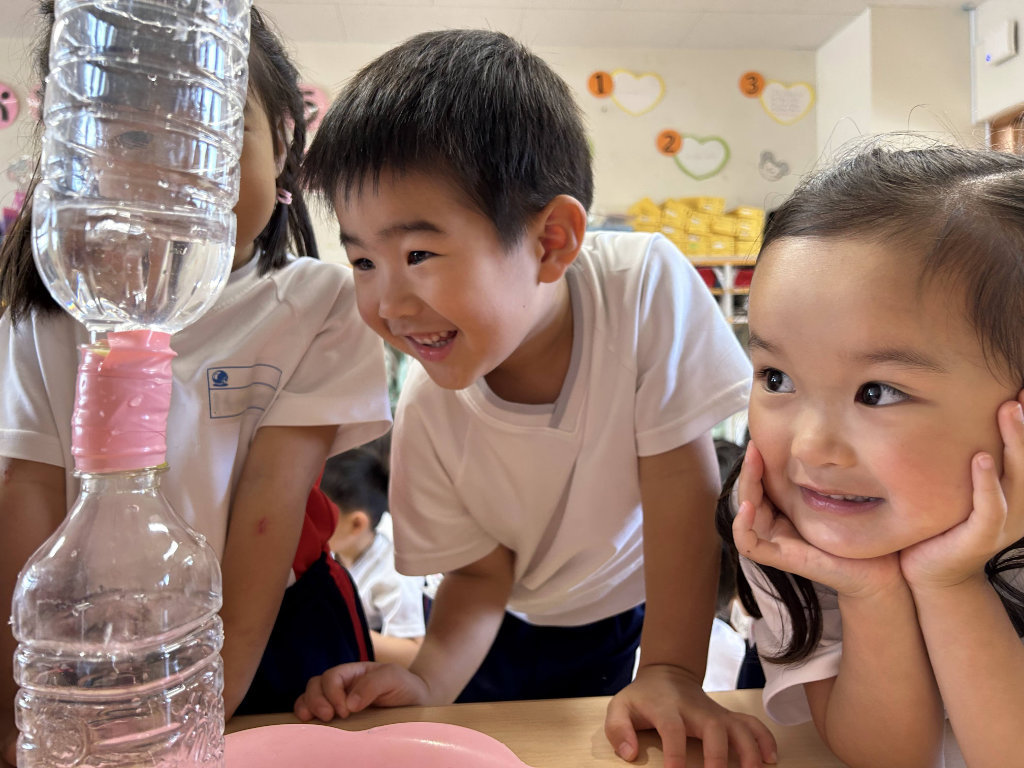 Children excitedly observe a STEAM experiment with water and plastic bottles in a classroom