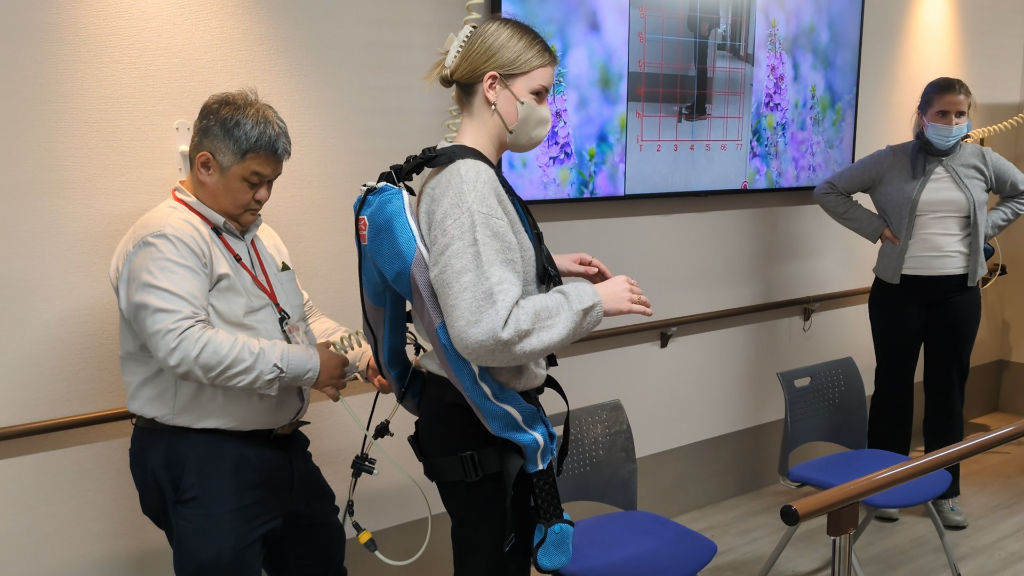 A staff member of Azalee Group adjusts a wearable muscle suit on a masked woman at Azalee Group's A-Cube facility.